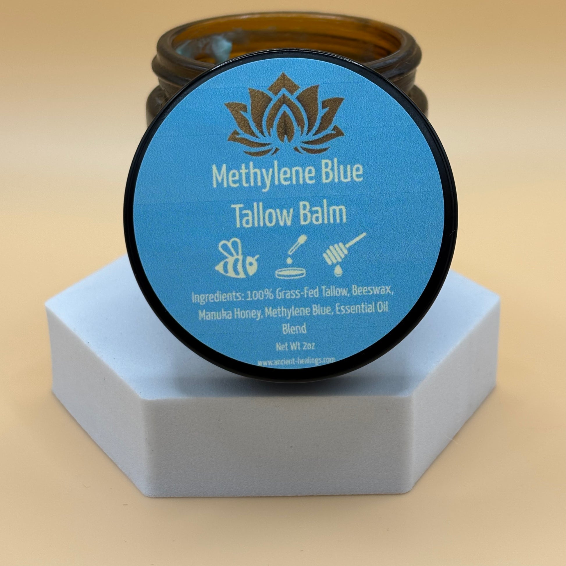 A jar of Methylene Blue Tallow Balm placed on a white surface, with a blue label on the lid that lists the ingredients and product name.